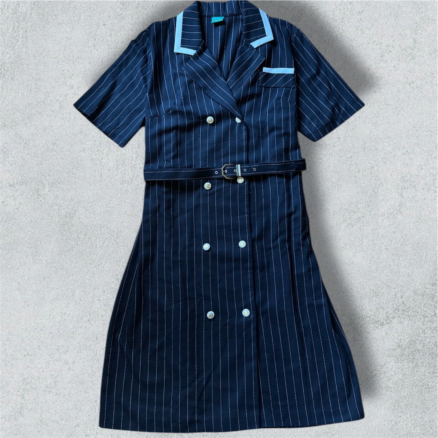 Navy pinstripe dress with white buttons on a light gray background